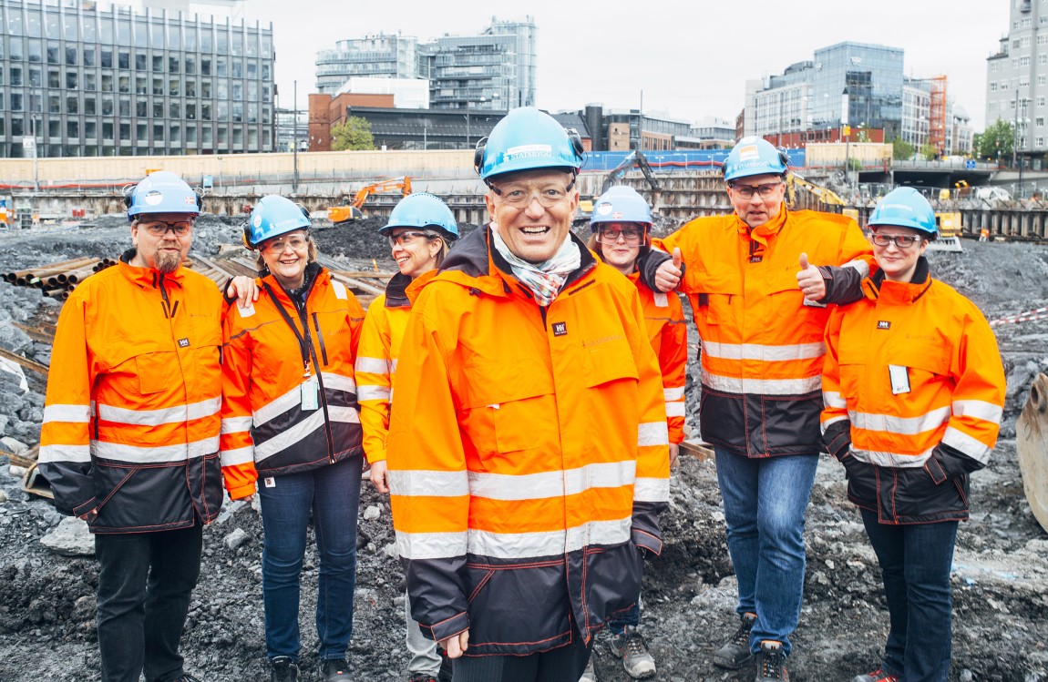 Mann i byggeklær omkranset av kolleger